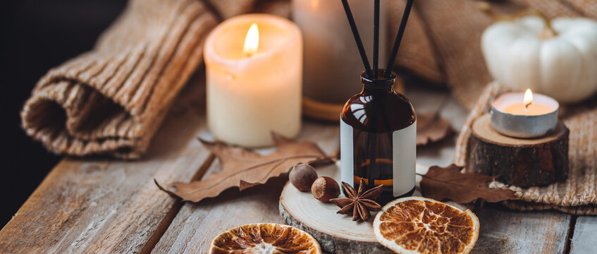 Concept of cozy fall home atmosphere, aromatherapy. Perfume, apartment aroma diffuser with autumn scent of pumpkin spicy sweet pie, cinnamon, anise. Room decor: pumpkins, dry orange, wool plaid banner