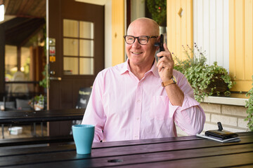 Happy Senior Man Outdoors in Restaurant Using Mobile Phone