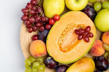 A plate filled with a variety of fruits, melon, apple, pear, grapes and peach on a light background. Top view, horizontal, free copy space.