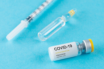 Coronavirus vaccine vial glass with a syringe on blue background.