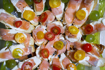 Top view of gourmet toasts with cream cheese, salmon, yellow and red cherry tomatoes, and green grapes