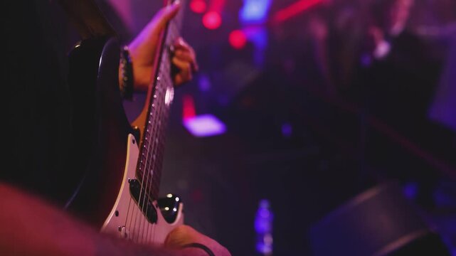 Concert view of an electric guitar player with vocalist and rock band performing in club, male musician guitarist on stage with audience in a crowded concert hall arena, live music show, slow motion
