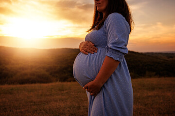 Pregnant woman at sunset, gently touching her belly