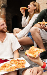 Vertical shot of happy young friends eating take away pizza in Italy. Diverse students friends...