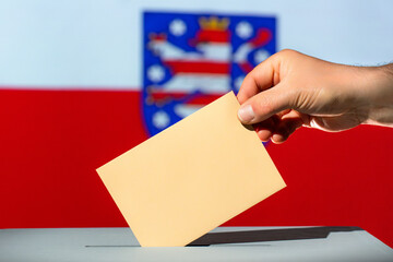 Voting envelope is put into ballot box for state election in Thuringia. Beige envelope in hand. Flag of Thuringia in the background. Election year 2024 in Germany.