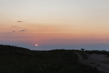 The breathtaking view of a sunset casts a warm glow over a vast field, with a winding dirt road meandering gracefully in the foreground