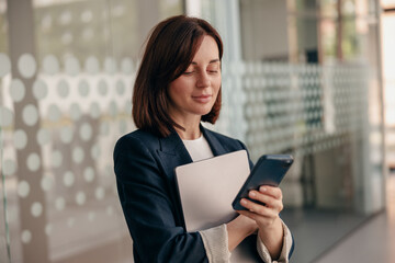 Confident businesswoman is focused on using her smartphone in a modern office setting