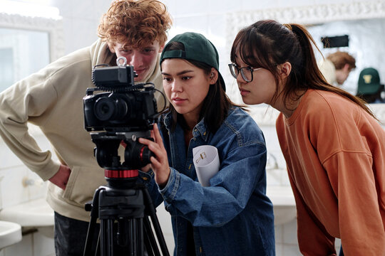 Group of young diverse individuals working together while setting up professional camera in modern studio environment. Enthusiastic team reviewing footage on camera screen