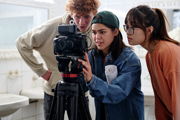 Group of young individuals gathered around camera, collaborating during filming process in bathroom...