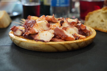 A delicious Typical feira octopus served on a wooden plate and with accompanying wine and bread.