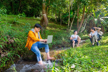 Asian businessman remote working online corporate business financial on laptop computer at camp in forest. People enjoy outdoor active lifestyle travel nature camping on summer holiday vacation.