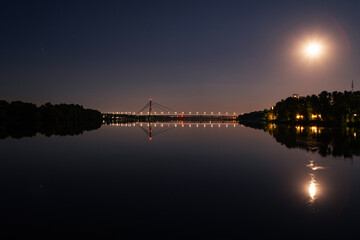 Kyiv, Ukraine - 17.08.2024: The Northern (moskow) Bridge against the background of the evening starry sky with reflection in the water. Obolon embankment. Pivnichny bridge.