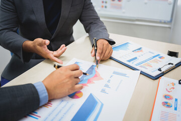 Asian business team engages in a collaborative meeting, financial charts at a desk. Dressed in formal suits, they brainstorm creative ideas to enhance company performance and team cohesion.