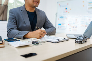 Asian business professional in a formal suit works at a desk, reviewing financial charts. manage car insurance claims, analyze auto loan options, sign lease agreements for vehicle transactions.