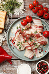 Slices of raw bacon, spices, tomatoes and bread on wooden table, flat lay