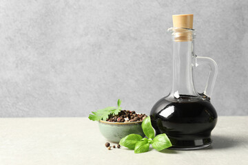 Balsamic vinegar in glass jug, herbs and spices on gray textured table, space for text