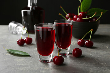 Delicious cherry liqueur in shot glasses and fresh berries on grey table