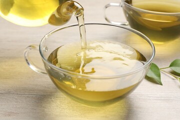 Pouring refreshing green tea into cup at wooden table, closeup