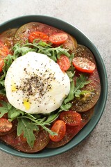 Delicious fresh burrata salad in bowl on gray textured table, top view