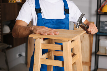 Man repairing wooden stool with hammer indoors, closeup
