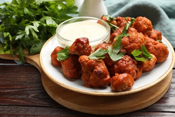 Baked cauliflower buffalo wings, parsley and sauce on wooden table, closeup