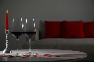 Burning candle, wine in glasses and paper hearts on table indoors. Space for text