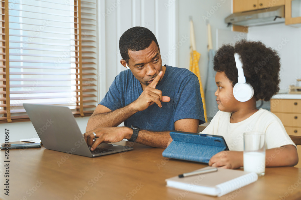 Wall mural black african american father working on laptop while son uses tablet with headphones at kitchen tab