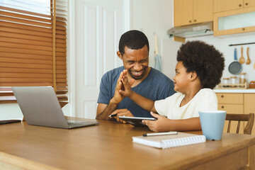 Black African American Father and son high five at kitchen table after using tablet, celebrating a successful bonding moment with technology.