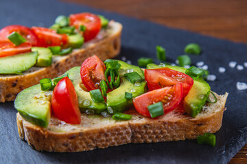 Avocado toast topped with tomato and green onion on a slice of carrot bread