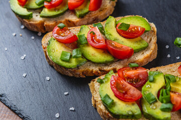 Avocado toast topped with tomato and green onion on a slice of carrot bread