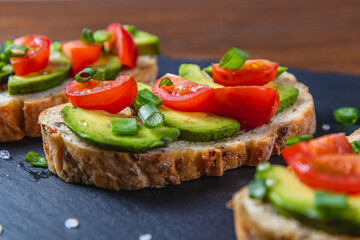 Avocado toast topped with tomato and green onion on a slice of carrot bread
