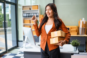 A beautiful businesswoman works at her desk, selling products online. She smiles while watching a tablet and talking on the phone. Her online business has exceeded sales targets, marking her success.