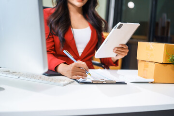 A beautiful businesswoman sits at the table, looking at the computer screen and talking on the phone. She analyzes marketing plans with a smile, feeling happy and successful in her online business.