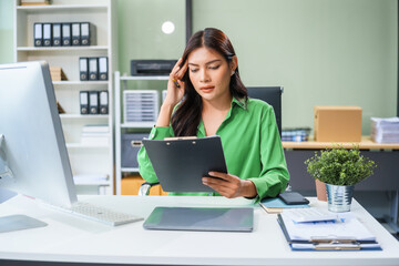 An Asian businesswoman sits at her office table, stressed and with a headache from hard work. Prolonged sitting leads to muscle weakness and the negative effects of office syndrome.