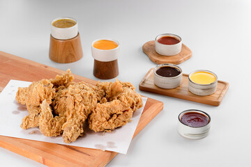 A stack of crispy fried chicken with various sauces around it.