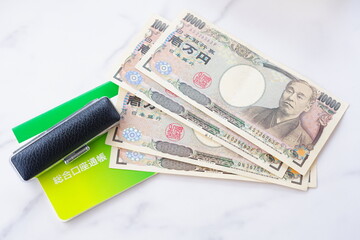 テーブルの上に置かれた銀行の預金通帳と印鑑、1万円札
