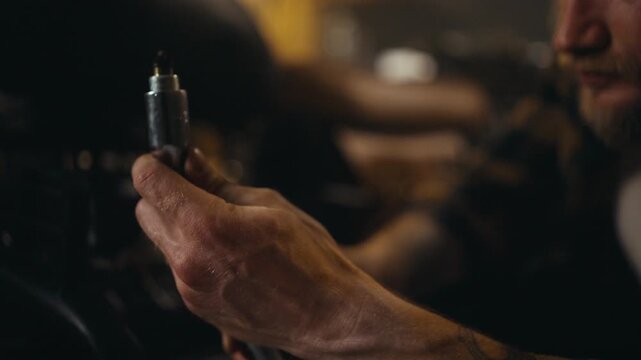 Close-up of a guy mechanic inspecting a spark plug while repairing a motorcycle and picking up tools in his workshop studio