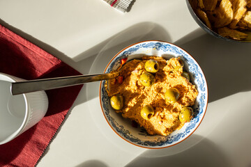Hummus in a bowl with olives and serving spoon.