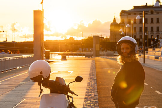 Stockholm, Sweden A woman stands next to a electric motor scooter with a helmet.