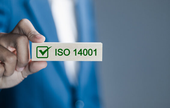 ISO 14001 concept. Businessman hold wooden block with icon of ISO 14001 certified for environmental management systems (EMS). Identify, control and reduce the environmental impact of activities.