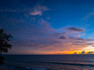 Obraz premium A captivating scene of a vibrant sunset casting an orange and purple glow across the sky, with gentle ocean waves lapping at the shoreline. The dramatic cloud formations add depth to the serene.