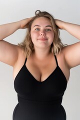 Fototapeta premium Young woman with blonde hair in a black bodysuit smiling against a white background.
