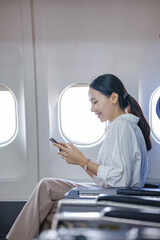 A woman is sitting on a plane and looking at her phone