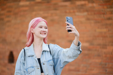 A girl with pink hair is taking a selfie with her cell phone