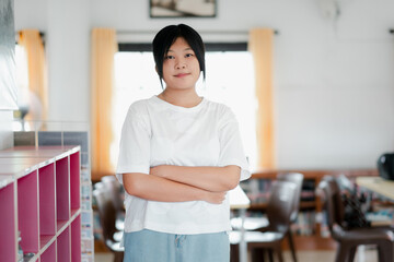 Obraz premium A young woman stands confidently in a bright, modern classroom with her arms crossed, exuding self-assurance and determination.
