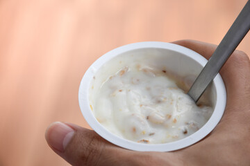 Close up a hand holding a glass of yogurt with Cereal cornflakes for breakfast on brown blurred background. Yogurt and cornflakes, Whole Grain, Granola, Muesli on a cup and spoon.