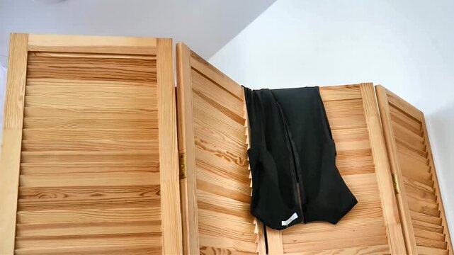 Close-up of a wooden screen behind that someone is changing and throwing clothes onto it