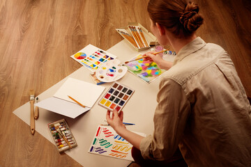 Woman painting with watercolors surrounded by art supplies