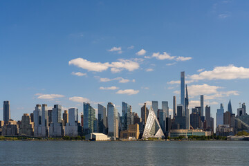 Naklejka premium Manhattan waterfront cityscape with modern skyscrapers under clear blue sky.
