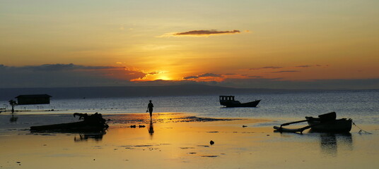 Die Sonne senkt sich am Walakiri Strand auf der Sumba Insel mit Booten und zeichnet letzte Silhouetten